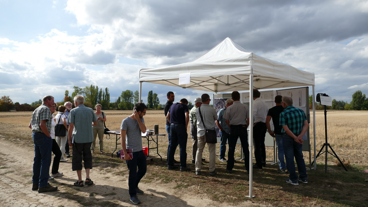 Eine Gruppe Menschen steht an einem Pavillon auf einem Feld